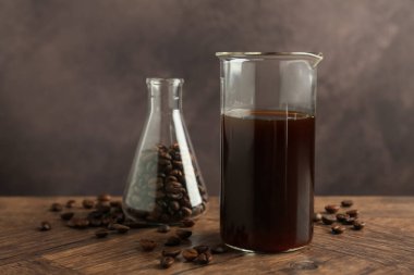 Kahverengi arka plana karşı ahşap masada kahve ve fasulye dolu cam deney şişesi.