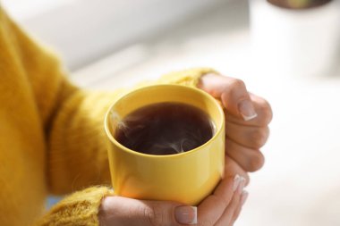 Sarı fincanı elinde tutan kadın, kapalı alanda çay içen, yakın plan.
