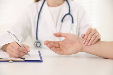 Doktor masadaki parmaklarıyla adamın nabzını kontrol ediyor.