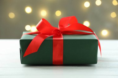 Beyaz ahşap masa üzerinde güzel bir Noel hediyesi kutusu. Arka planda bulanık ışıklar var. Yakın plan.