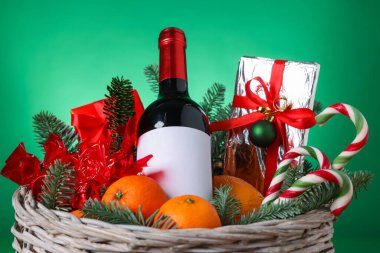 Bir şişe şarap, köknar ağacı dalları, sepetteki şeker ve mandallar yeşil arka planda, yakın plan. Kutlama hediyesi.