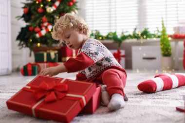 Noel hediyesi olan şirin bir bebek. Şenlikli bir odada yerde. Mesaj atmak için yer var.