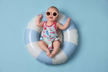 Şişirilebilir halkada güneş gözlüklü şirin bir bebek açık mavi arka planda, üst tarafta.