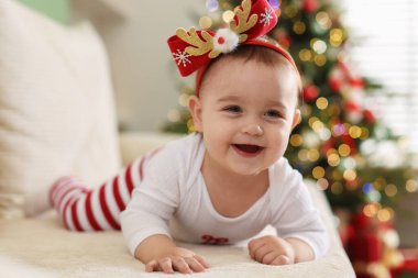 Evdeki kanepede şirin bir Noel bandı takan küçük bebek.