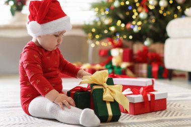 Evde yerde hediyeleri olan Noel Baba şapkalı şirin bir çocuk. Bebeğin ilk Noel 'i