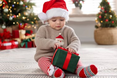 Evde yerde Noel Baba şapkası ve hediyesiyle küçük şirin bir bebek. Noel sezonu