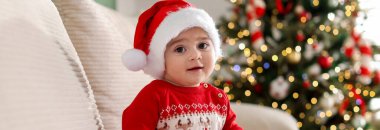 Evdeki kanepede Noel Baba şapkalı şirin bir bebek. Noel sezonu