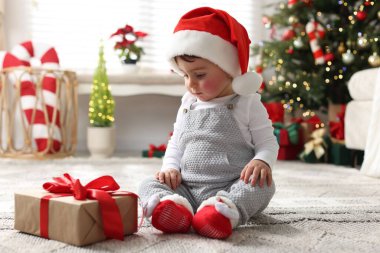 Noel Baba şapkalı küçük çocuk Noel için dekore edilmiş odada yerde hediyeyle