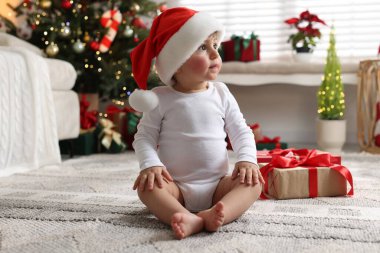 Noel Baba şapkalı küçük çocuk Noel için dekore edilmiş odada yerde hediyeyle