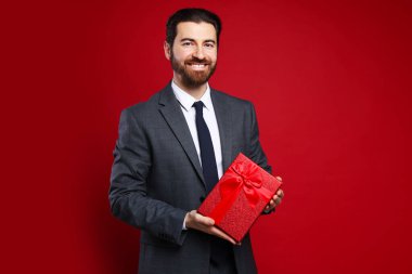 Sevgililer Günü. Kırmızı arka planda hediyesi olan yakışıklı bir adam.