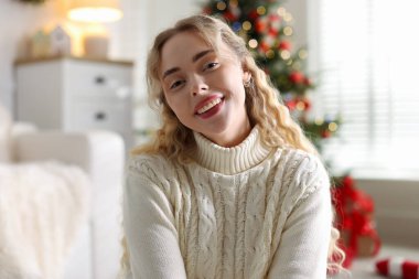 Evdeki bulanık ışıklara karşı süveter giymiş gülümseyen kadın portresi. Mutlu Noeller ve mutlu yıllar.