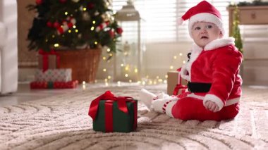 Noel Baba kostümlü şirin bir bebek ve evde yerde Noel hediyeleri.