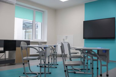 Okulda masaları, sandalyeleri ve televizyonu olan şık bir sınıf.