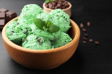Yummy mint chocolate chip ice cream in bowl on black wooden table, closeup. Space for text