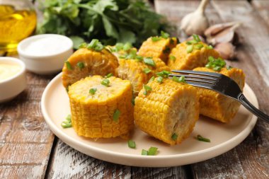 Haşlanmış mısır koçanları ve yeşil soğanlar ahşap masada servis ediliyor.