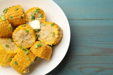 Yeşil soğan ve tereyağlı haşlanmış mısır koçanı parçaları açık mavi ahşap masa, üst manzara. Metin için boşluk