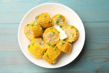 Yeşil soğanlı haşlanmış mısır koçanları ve açık mavi ahşap masada tereyağı.