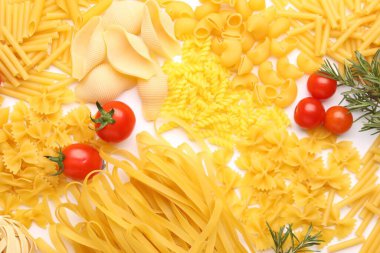 Farklı türde çiğ makarna, domates ve biberiye beyaz masada, düz yerde.