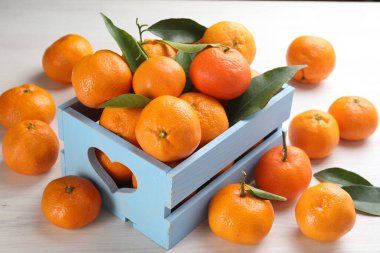 Beyaz ahşap masada taze mandalina ve yeşil yapraklar.