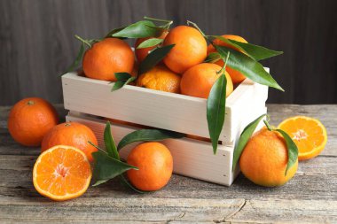 Tahta masadaki sandıkta taze mandalinalar ve yeşil yapraklar, yakın plan.