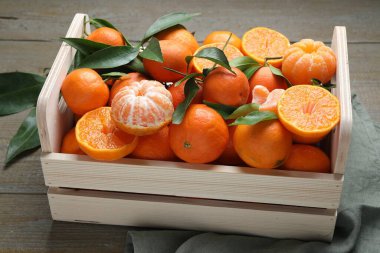 Tahta masadaki sandıkta taze mandalinalar ve yeşil yapraklar, yakın plan.