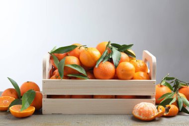 Tahta masadaki sandıkta taze mandalina ve yeşil yapraklar.