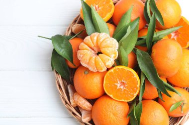 Taze mandalinalar ve sepetteki yeşil yapraklar beyaz ahşap masa, üst manzara. Metin için boşluk