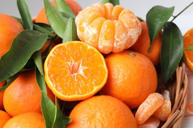 Taze mandalinalar ve sepetteki yeşil yapraklar masada, yakın plan.