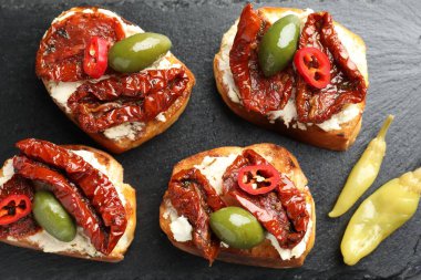 Krem peynirli lezzetli bruschettalar, güneşte kurutulmuş domatesler, acı biber ve siyah desenli masada yeşil zeytinler, düz uzanmış