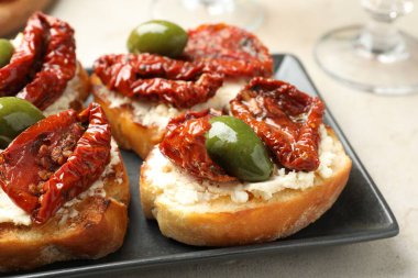 Krem peynirli lezzetli bruschettalar, güneşte kurutulmuş domatesler ve gri masada yeşil zeytinler, yakın plan.