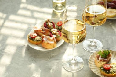 Bardakta beyaz şarap, gri masada esmer ve aperatifler.