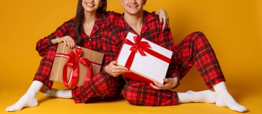 Komik saç bantları ve turuncu arka planda Noel hediyeleri olan pijamalı mutlu bir çift.