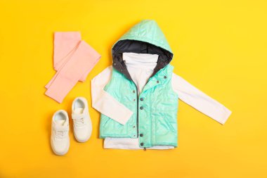 Düz kompozisyon, şık çocuk kıyafetleri ve sarı arka planda ayakkabılar.