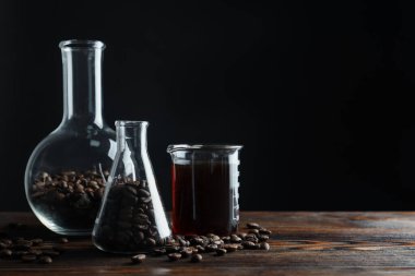 Siyah arka planda kahve, fasulye ve beher kaplı cam mataralar, yakın plan. Metin için boşluk