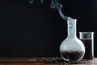 Kahve, fasulye ve beher dumanlı cam matara siyah arka planda, yakın plan. Metin için boşluk