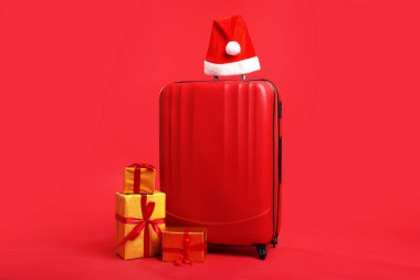 Noel Baba şapkalı bavul ve kırmızı arka planda hediyeler. Noel tatili