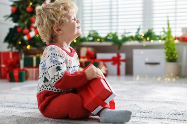 Noel hediyesi olan şirin bir bebek. Şenlikli bir odada yerde. Mesaj atmak için yer var.