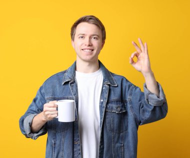 İçkili yakışıklı genç adam sarı arka planda iyi bir jest gösteriyor.