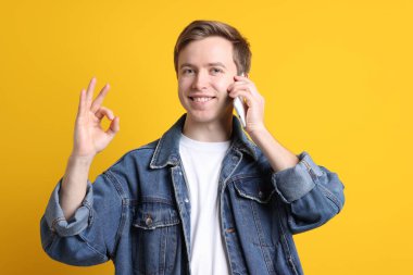 Yakışıklı genç adam telefonda konuşuyor ve sarı arka plana karşı iyi bir hareket gösteriyor.