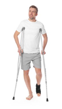 Beyaz arka planda yaralı bacağı ve koltuk değneği olan bir adam.