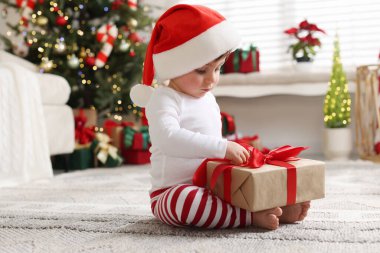 Noel Baba şapkalı küçük çocuk Noel için dekore edilmiş odada yerde hediyeyle