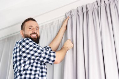 Evde pencere perdelerini asan adam, düşük açılı görüntü.