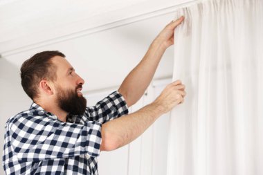 Evde pencere perdelerini asan adam, düşük açılı görüntü.