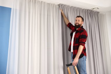 Evde perdeleri asan merdivenli bir adam var. Düşük açılı. Metin için boşluk