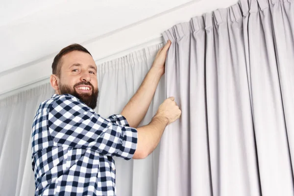 Evde pencere perdelerini asan adam, düşük açılı görüntü.