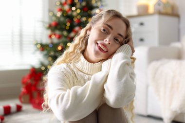 Evdeki bulanık ışıklara karşı süveterli, gülümseyen kadın. Mutlu Noeller ve mutlu yıllar.