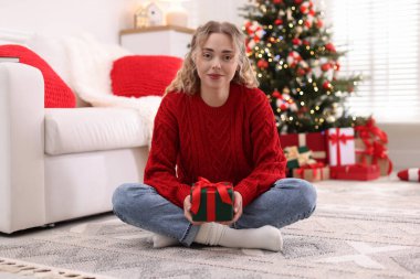 Evde bulanık ışıklara karşı Noel hediyesi giymiş güzel bir kadın.