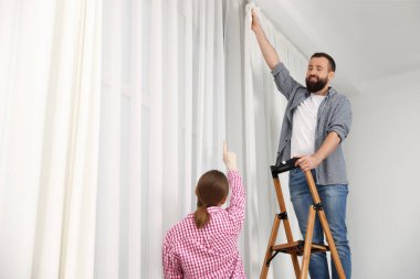 Evde pencere perdelerini asan merdivenli bir çift var. Düşük açılı. Metin için boşluk