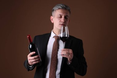 Profesyonel şarap garsonu kahverengi arka planda kırmızı şarap tadıyor.