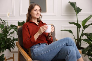 Evdeki koltukta bir fincan aromatik kahveli kadın.